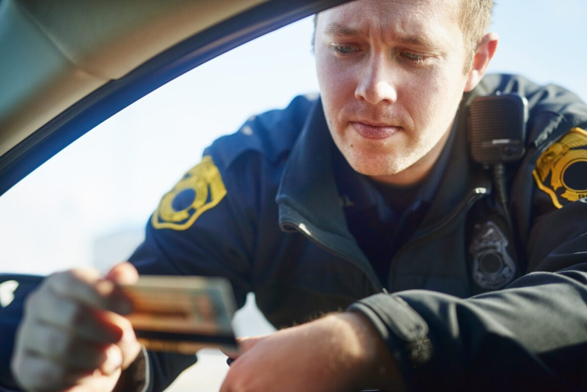 Law enforcement officer looks at drivers license, hold license in his hands as he leans through open window